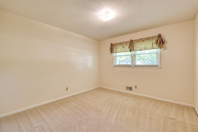 spare room with baseboards, a textured ceiling, visible vents, and light colored carpet