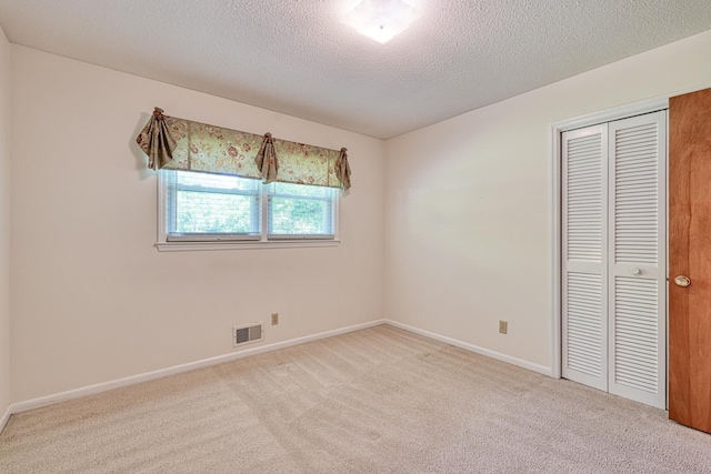 unfurnished bedroom with a textured ceiling, carpet flooring, a closet, and visible vents