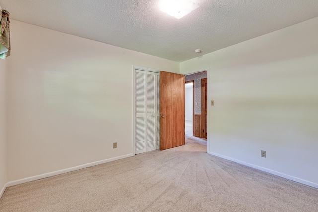 empty room with a textured ceiling, baseboards, and light colored carpet
