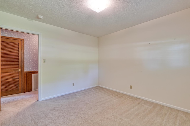 spare room with carpet flooring, a textured ceiling, visible vents, and wainscoting
