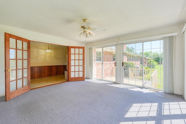 empty room with carpet flooring, a textured ceiling, wooden walls, and ceiling fan