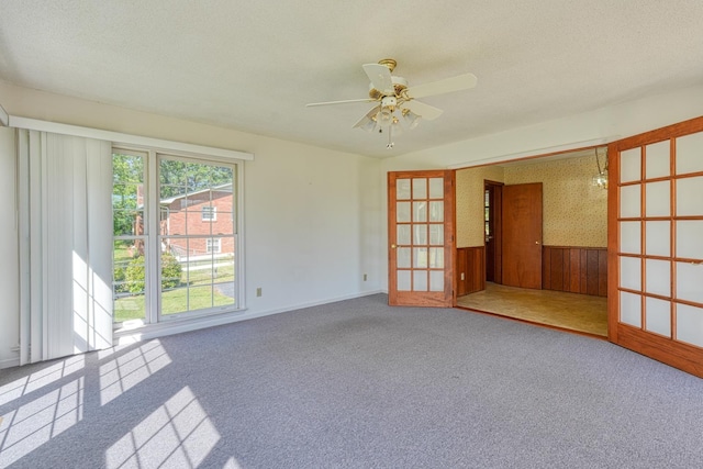 carpeted empty room with a ceiling fan, wooden walls, wainscoting, and baseboards