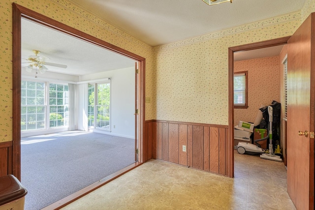 interior space with a wainscoted wall, a ceiling fan, and wallpapered walls
