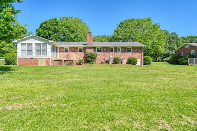 rear view of property featuring brick siding, a chimney, and a lawn