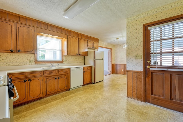kitchen with a sink, wallpapered walls, light floors, wainscoting, and white appliances