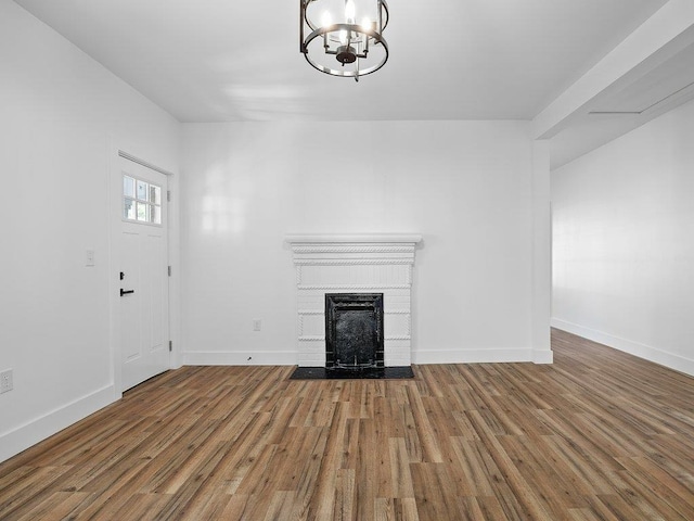 unfurnished living room with baseboards, a chandelier, wood finished floors, and a fireplace