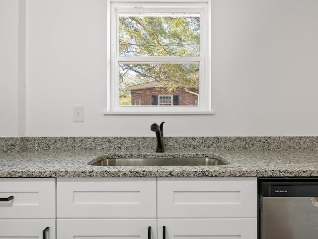 kitchen with white cabinetry, stainless steel dishwasher, light stone counters, and a sink