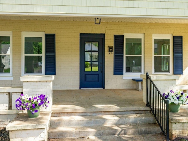 property entrance with a porch and brick siding