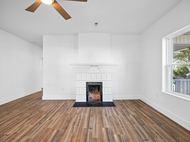 unfurnished living room featuring a brick fireplace, wood finished floors, visible vents, and ceiling fan