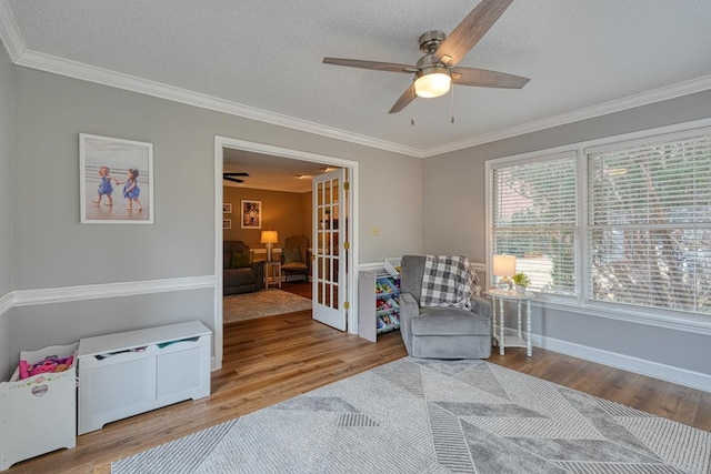 sitting room with ceiling fan, wood finished floors, french doors, ornamental molding, and a textured ceiling
