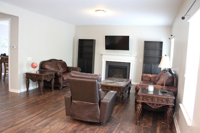 living room with dark wood-style flooring, a glass covered fireplace, and baseboards