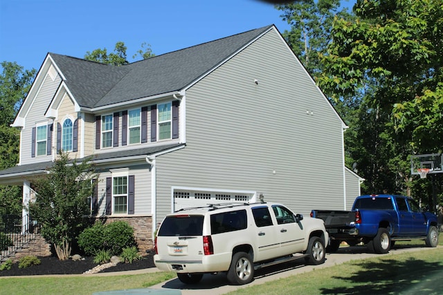 view of side of home featuring an attached garage and a shingled roof