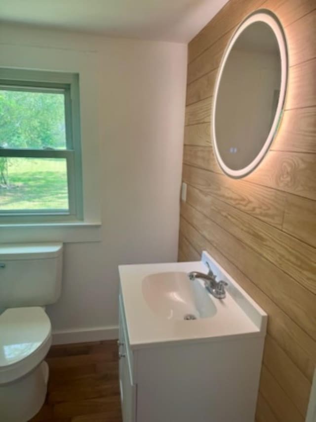 half bathroom featuring wooden walls, wood finished floors, toilet, vanity, and baseboards
