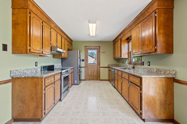 kitchen featuring stainless steel appliances, under cabinet range hood, a sink, baseboards, and brown cabinets