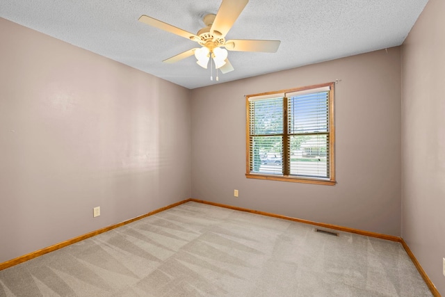 spare room with light colored carpet, baseboards, ceiling fan, and a textured ceiling