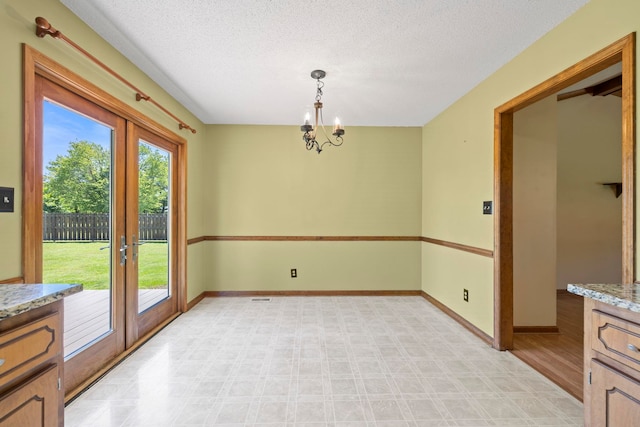 unfurnished dining area with french doors, a textured ceiling, baseboards, a chandelier, and light floors