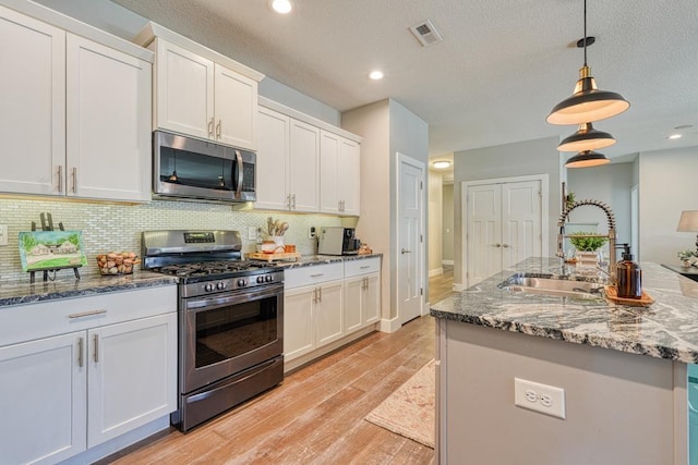 kitchen featuring appliances with stainless steel finishes, a sink, light wood-type flooring, white cabinetry, and backsplash
