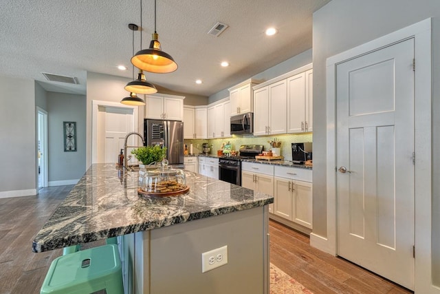 kitchen featuring appliances with stainless steel finishes, white cabinetry, wood finished floors, backsplash, and recessed lighting