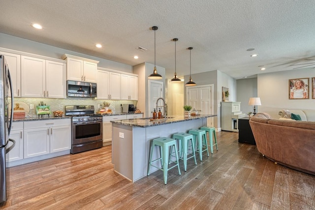 kitchen with appliances with stainless steel finishes, a sink, light wood-type flooring, open floor plan, and a kitchen bar