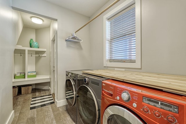clothes washing area with washing machine and clothes dryer, wood finished floors, and baseboards