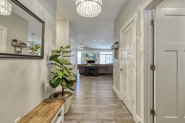 hall featuring a chandelier, wood finished floors, and a textured ceiling
