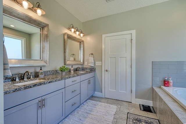 full bath with baseboards, double vanity, tiled bath, and a textured ceiling