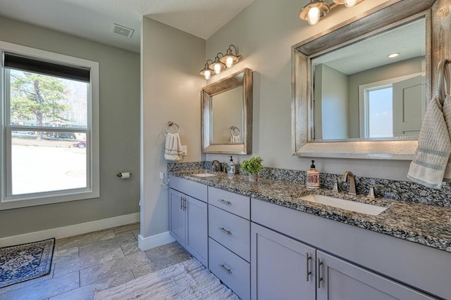 full bathroom featuring baseboards, plenty of natural light, stone tile flooring, and double vanity