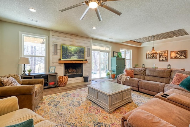 living room featuring a textured ceiling, light wood-style flooring, a ceiling fan, a fireplace, and a chandelier