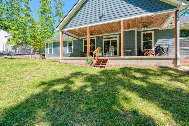 rear view of property with a trampoline and a lawn
