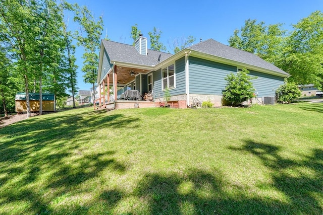 back of property featuring a ceiling fan, a chimney, central AC, and a yard