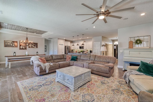 living room featuring baseboards, a chandelier, ceiling fan, light wood-type flooring, and a textured ceiling