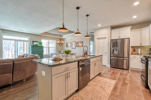 kitchen with stainless steel appliances, open floor plan, light wood finished floors, dark stone countertops, and recessed lighting