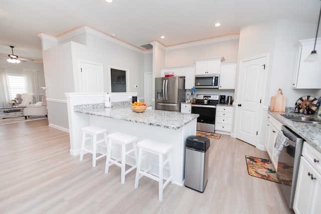 kitchen with stainless steel appliances, a kitchen bar, light wood-type flooring, white cabinets, and crown molding