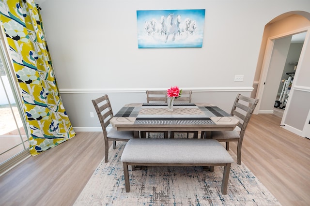 dining room with wood finished floors, arched walkways, and baseboards