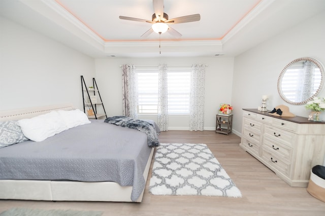 bedroom featuring a raised ceiling, crown molding, light wood-style floors, baseboards, and ceiling fan