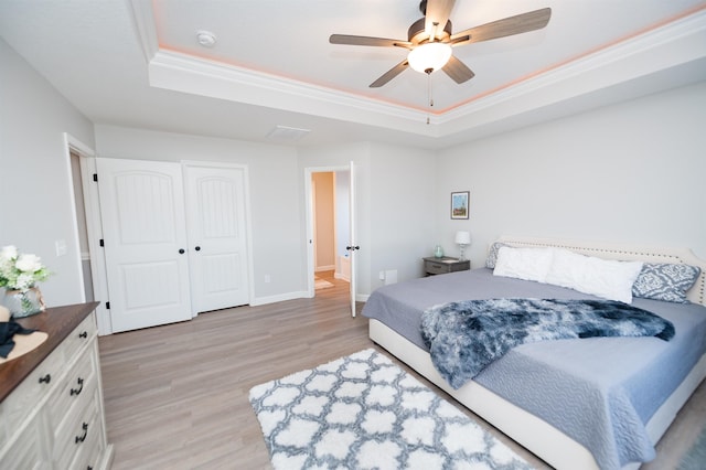 bedroom featuring a raised ceiling, light wood-style flooring, a ceiling fan, ornamental molding, and baseboards