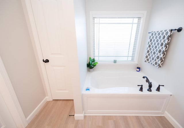 full bath featuring wood finished floors, a garden tub, and baseboards