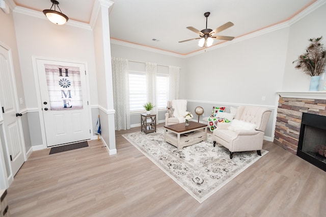 living room with light wood-type flooring, ornamental molding, ceiling fan, a fireplace, and baseboards