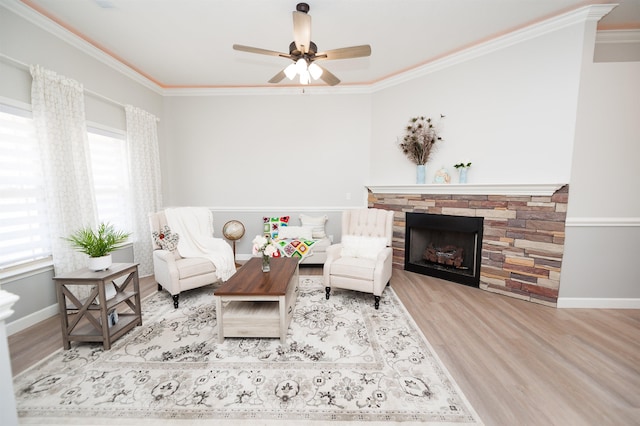 living room featuring wood finished floors, ornamental molding, a ceiling fan, a stone fireplace, and baseboards