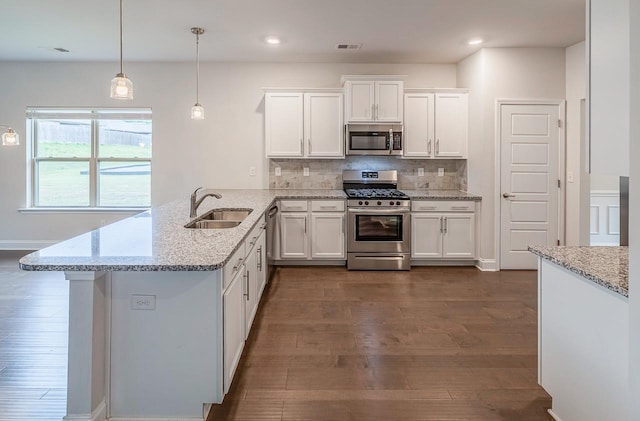 kitchen featuring appliances with stainless steel finishes, a sink, dark wood-style floors, a peninsula, and white cabinets