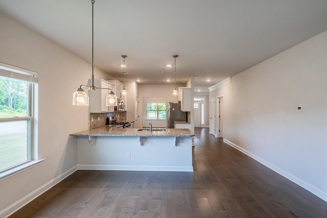 kitchen with appliances with stainless steel finishes, a peninsula, a sink, white cabinets, and baseboards