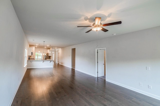 unfurnished living room with a ceiling fan, dark wood-style floors, and baseboards