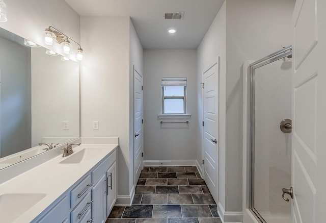 full bath featuring a shower stall, baseboards, double vanity, recessed lighting, and stone finish flooring