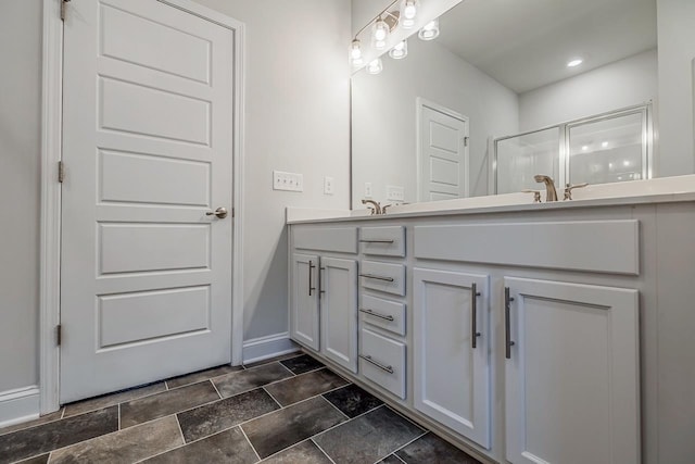 bathroom featuring double vanity, baseboards, a shower with door, and stone finish flooring
