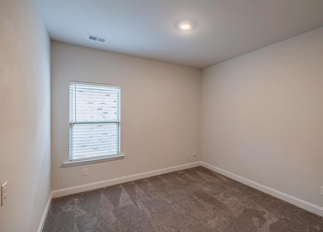 spare room featuring dark carpet and baseboards