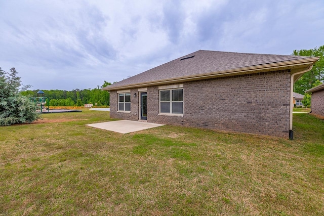 rear view of house with a patio area, a yard, brick siding, a playground, and roof with shingles