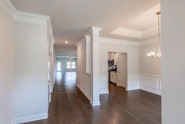 hallway featuring dark wood-style flooring, crown molding, a wainscoted wall, a chandelier, and a decorative wall