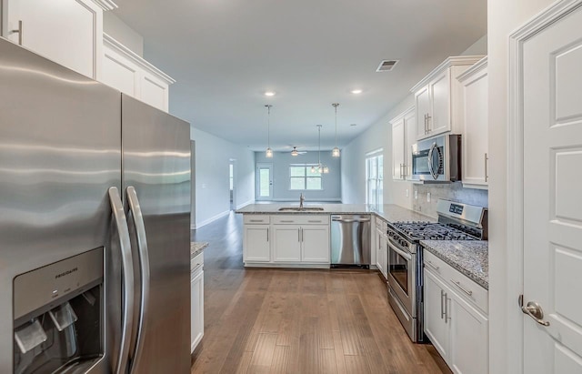 kitchen with appliances with stainless steel finishes, a sink, a peninsula, recessed lighting, and white cabinetry