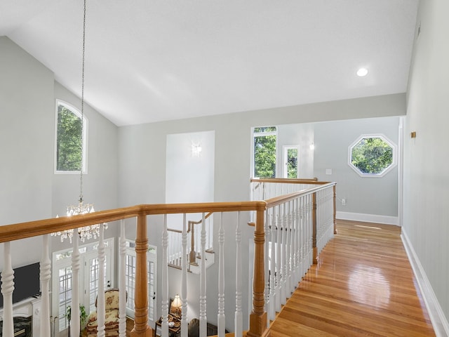 hall with light wood finished floors, plenty of natural light, a chandelier, baseboards, and vaulted ceiling