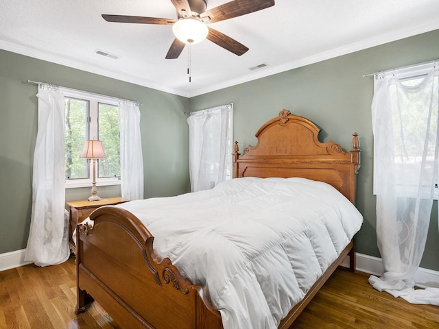 bedroom with baseboards, wood finished floors, ornamental molding, and ceiling fan